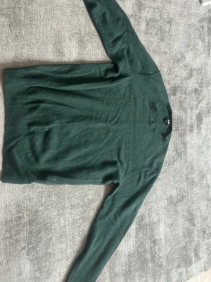 Mörkgrön stickad tröja - Mysig mörkgrön stickad tröja med rund hals och långa ärmar. Enkel och stilren design som passar perfekt till jeans eller kjol. Tröjan har en mjuk känsla och är lätt att matcha med olika outfits.