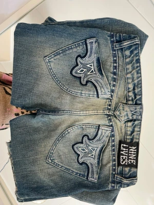 Low waist Nine Lives blå jeans med brodyr - Säljer mina nine lives jeans pga att jag har växt ur de! Köpta på sellpy💕 de är straight med en slits (se på bilderna) som jag gjort själv så de ska bli lite mer bootcut! Lite slitningar där nere men annars jättefint skick!
