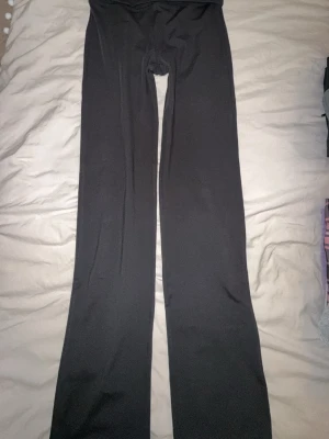 Svarta bootcut träningsbyxor  - Bootcut träningsbyxor i svart med bred, vikbar midja och diskret logotyp på höften. Materialet är stretchigt och mjukt, perfekt för träning. 