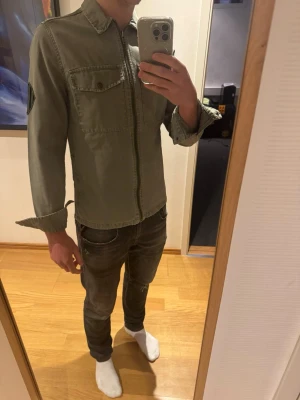 Grön overshirt från ZARA - Olivgrön overshirt från Zara köpt för 999kr, bra skick utöver ett litet slitage i armhålan som inte syns med den på, går och laga lätt. 