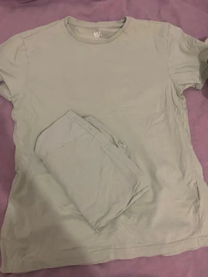 Ljusgrå pyjamas-set i bomull - Mjuk och enkel ljusgrå pyjamas med kortärmad t-shirt och matchande byxor. Tillverkad i bomull för en bekväm känsla. Perfekt för slappa dagar hemma eller en god natts sömn.