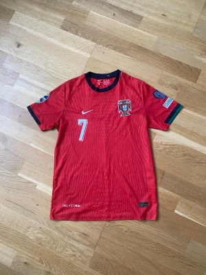 Portugal matchtröja Nike röd - Röd Portugal matchtröja från Nike med nummer 7 på bröstet, landslagets emblem och svarta detaljer vid krage och ärmslut. Tillverkad i lätt funktionsmaterial med Dri-FIT-teknologi. Perfekt för fotbollsträning eller att bära som supporter.
