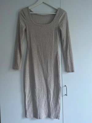 Beige ribbad långklänning - Säljer en beige ribbad långklänning med rundad, djup halsringning och långa ärmar. Klänningen har en kroppsnära passform och är tillverkad i ett stickat material som känns mjukt och bekvämt. Strechig.