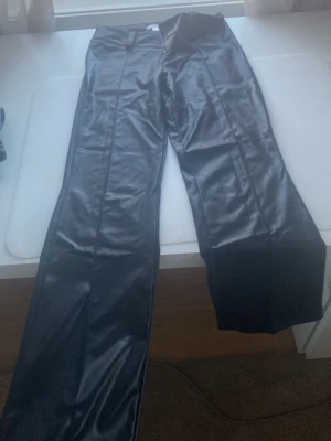 Svarta fuskskinnbyxor Gina Tricot - Säljer ett par svarta byxor i fuskskinn från Gina Tricot. Byxorna har raka ben, låg midja och dragkedja i mitten . Snygg glansig finish som ger en cool look. Perfekta för dig som vill sticka ut lite extra.