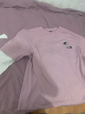 Ljusrosa t-shirt från Dickies - Säljer en ljusrosa t-shirt med klassisk logga på bröstet. T-shirten har rund halsringning och korta ärmar. Perfekt för dig som gillar streetwear och vill ha en enkel men snygg look.