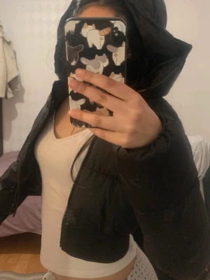 Svart croppad pufferjacka med huva - Säljer en svart croppad pufferjacka med stor huva och dragkedja framtill. Jackan har en boxig passform och är perfekt för kalla dagar. Enkel, stilren design utan synliga loggor eller detaljer. Passar dig som vill ha en trendig och varm vinterjacka.