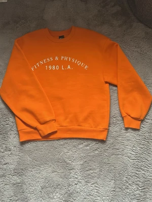 Orange sweatshirt  - Cool orange sweatshirt med tryck i vitt på bröstet. Tröjan har rund hals, ribbade muddar och är gjord i mjukt material, perfekt för en avslappnad streetwear-look. Köpt på Gina tricot för ca 1år sedan, säljer då den aldrig har kommit till användning. :))
