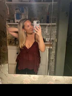 Vinröd volang linnetopp - Säljer en vinröd linnetopp med volangdetaljer och v-ringning. Toppen är andvänd bara en gång och köpt från bikbok passar s-L