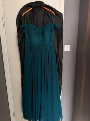 Mörkgrön balklänning med spetsdetaljer - Säljer nu min mörkgröna balklänning. Färgen är huntergreen och gör sig inte riktigt rättvis på bild. Balklänningen är uppsydd för att passa någon som är ca 167-172 beroende på hur höga skor som används. Klänningen är i storlek UK 14 vilket motsvarar storlek 42. Priset är diskuterbart. Klänningen är inköpt på dream designs i Motala.