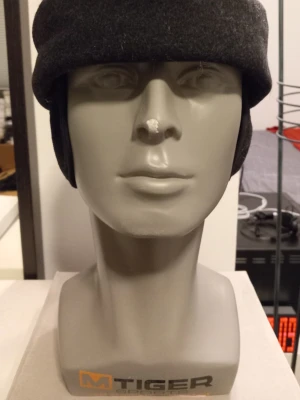 Svart Mössa från Shaman - Storlek 57 - Stilren svart mössa från Shaman i mjuk ull. Mössan har en enkel design med en liten metallbricka med logga på sidan. Perfekt för dig som vill ha en klassisk look med en modern touch.