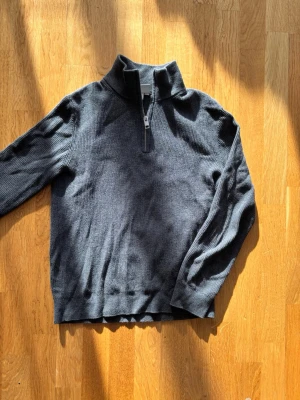 Mörkgrå stickad halfzip från H&M - Mörkgrå stickad tröja från H&M i slim fit-modell. Tröjan har en hög krage med dragkedja (halfzip) och ribbstickad struktur. Perfekt för lager på lager och enkel att styla till olika outfits.