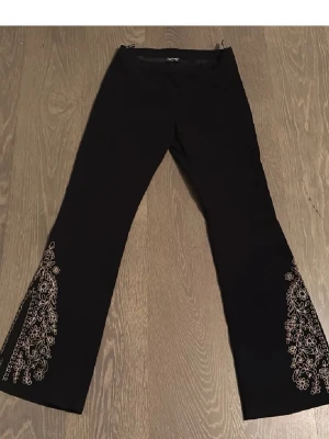 Svarta vintage Coolaaa byxor😊 - Snygga svarta byxor från Miss Etam med vackra broderade blommor i guld längs benen. Perfekta för en festlig kväll eller när du vill känna dig extra fin. Byxorna har en elegant bootcut-stil mocca tyg som ger en smickrande siluett. De är i mycket bra skick och redo att bäras till nästa event! Midjemått ca 36cm innerbenslängd 83cm