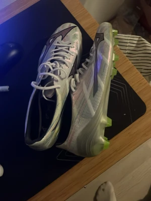 Vita Mizuno fotbollsskor med neon-dobbar - Säljer ett par vit/gröna Mizuno fotbollsskor dem är i väldigt gott skick( aldrig använda )  PRISET ÄR EJ HUGGET I STEN!