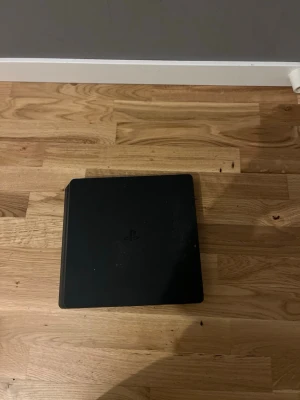 PlayStation 4 Slim svart konsol - Säljer en svart PlayStation 4 Slim från Sony. Konsolen har en stilren, rektangulär design med rundade hörn och matt finish. Perfekt för gaming och streaming. Klassisk PS4-logga på ovansidan. Passar dig som vill ha en smidig och snygg spelkonsol. Jag har Fc 25 Fc 24 och nba 2k 26. Jag kan erbjuda hdmi kabel.
