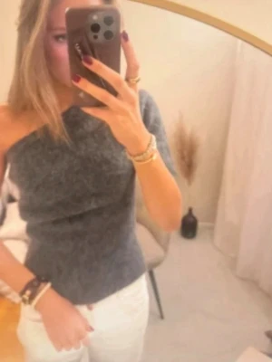 Mörkgrå stickad oneshoulder topp - Säljer en snygg mörkgrå stickad topp med oneshoulder-design. Toppen har en mjuk och fluffig känsla och passar perfekt för dig som vill ha något trendigt och bekvämt. Enkel att matcha med jeans eller kjol. Storlek L men passar S/M