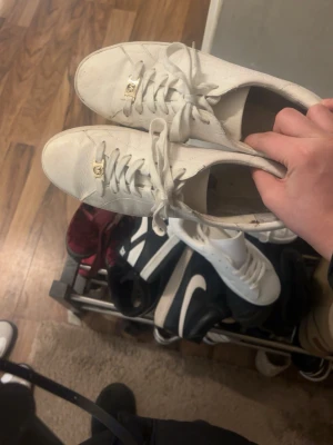 Vita Michael Kors sneakers - Stilrena vita sneakers från Michael Kors med gulddetaljer på snörningen och diskret logga på sidan. Skorna har lågt skaft och är tillverkade i läder med mönstrad struktur. Perfekta för dig som gillar klassisk och clean stil.