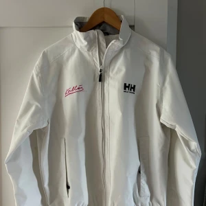 Helly Hansen jacka, kallis - Snygg vit Helly Hansen jacka med sommarklubben kallis på Gotlands logga på. Jackan är i fint skick. 