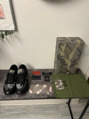 Valentino Garavani camo sneakers - Snygga sneakers från Valentino Garavani med svart och grått camo-mönster. Dom är använda en gång . Skorna har mesh- och läderdetaljer, svarta skosnören och logga på plösen. Perfekt för dig som vill sticka ut med exklusiva och trendiga sneakers.