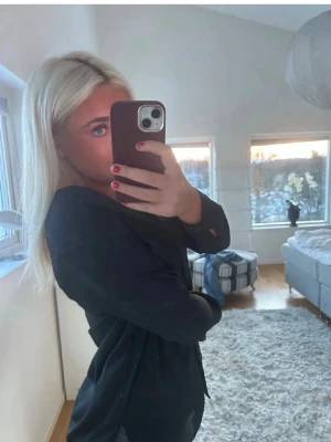 Svart långärmad blus - Stilren svart blus med lång ärm och avslappnad passform. Blusen har en lätt glansig yta och v-ringad halsringning. Perfekt att matcha med jeans eller kjol för en trendig look.