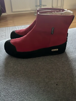 Röda boots från Bally - Säljer ett par röda boots från Bally med svart sula och tåparti. Bootsens insida är fodrad med mjukt, vitt material för extra värme. De har en klassisk, hög siluett och tydliga Bally-loggor på sidan. Perfekta för kalla vinterdagar och riktigt snygga till vinterlooken.