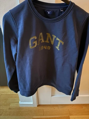 Mörkblå Gant sweatshirt  - Mörkblå Gant sweatshirt med guldig text! Barnstorlek L. Passar 160-170cm! Nästan helt ny, använd ett fåtal gånger! Nypris 999 kr! Mitt pris 349 kr! Inga defekter! Kan köpas tillsammans med några av mina andra kläder. Pris kan diskuteras vid snabb o enkel affär. Tveka inte på att höra av er om ni är intresserade!