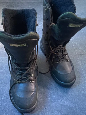 Svarta vinterkängor från Chiruca hunter - Tuffa svarta vinterkängor från Chiruca hunter  med högt skaft, grov sula och snörning hela vägen upp. Insidan är fodrad med mjukt material för extra värme. Perfekta för kalla dagar och outdoor-äventyr. Metallhål för snörning och slitstark ovandel.