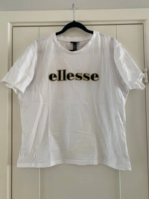 Vit ellesse t-shirt med broderad logga XL - Säljer en vit t-shirt från ellesse i storlek XL. T-shirten har korta ärmar och ett stort broderat ellesse-tryck i svart med guldkant på bröstet. Tillverkad i mjuk bomull och har en klassisk rund hals. Perfekt för en clean och sportig look. Förutom ett par ljusare fläckar efter deo i armhålan är tröjan i väldigt fint begagnat skick   Mått Över bröstet: ca 55 cm Längd från axeln och ner: ca 61 cm  100% bomull   Kommer från ett djur och rökfritt hem