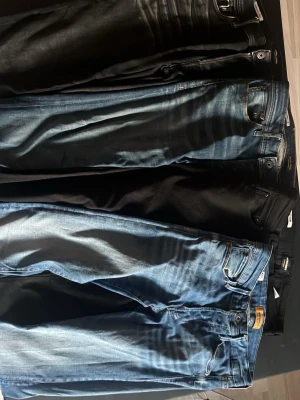 Svarta och blå jeans från Jack & Jones - Säljer flera par jeans från Jack & Jones i både svart och blå tvätt. Klassisk femficksmodell med knappgylf och bekväm passform. Perfekta för dig som gillar en avslappnad men ändå stilren look. Materialet är slitstarkt denim. Den längst åt vänster på den första bilden är 29/32 sen 30/32 och de sista två är bara använda ett fåtal gånger och är båda 27/32 både de sista för 599kr eller en av dem för 399kr styck dem andra för 299kr styck allt för 100kr..
