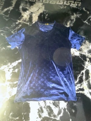 Blå sammetst-shirt  - Snygg mörkblå t-shirt i sammet från  med diskret mönster över hela plagget. T-shirten har rund halsringning och korta ärmar. Perfekt för dig som vill sticka ut med en lyxig och unik look.