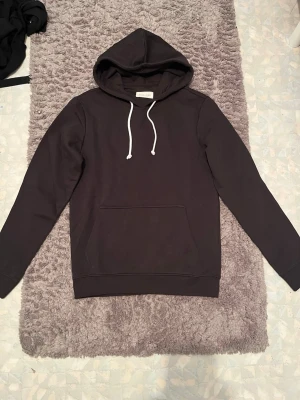 Svart hoodie från Pier One - Snygg svart hoodie från Pier One med klassisk huva och vita dragsnören. Hoodien har en stor magficka framtill och är tillverkad i mjukt bomullsmaterial som känns skönt mot huden. Perfekt för en avslappnad och stilren look.