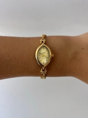 Vintage klocka - (OBS! INTE BEGAGNAD, FINNS ÄVEN ATT BESTÄLLA VIA HEMSIDAN byomé.se)  Vintage inspirerad guldfärgad klocka – helt vattentålig och så unik! Skick: NY! Klockans längd: ca 19 cm – kan justeras mindre genom att ta bort länkar Urtavlans storlek: ca 1,9 cm. Finns i begränsat antal!