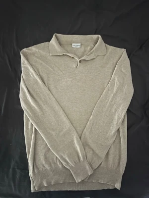 Beige stickad tröja John Henric - Snygg beige stickad tröja från John Henric med klassisk krage och långa ärmar. Tröjan har ribbade muddar vid ärmslut och nederkant, perfekt för en stilren och enkel look. Tillverkad i mjukt material som känns skönt mot huden.