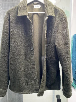 Fleece jacka - Mysig olivgrön teddyjacka från Envii med klassisk krage och knäppning framtill. Jackan har en avslappnad passform, långa ärmar och är gjord i mjukt teddy-material som håller dig varm. Perfekt för kyliga dagar och enkel att styla till olika outfits.