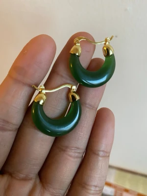 s925 jadeGröna hoops med gulddetaljer - Snygga örhängen i form av gröna hoops med guldfärgade detaljer. De har en rundad, tjock design och stängs med klassisk bygel. Materialet ser ut som grön sten eller resin kombinerat med metall i guldfärg. Perfekta för dig som vill sticka ut lite extra.s925 sterling silver plated and green part jade