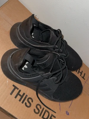 Svarta Adidas sneakers med snörning - Snygga helsvarta sneakers från Adidas med klassiska tre ränder på sidan. Skorna har en sportig siluett, ovandel i mesh och syntet samt snörning för perfekt passform. Perfekta för dig som gillar stilrena och bekväma sneakers. Storlek 40 