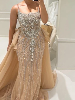 Champagnefärgad långklänning med pärlor - Magisk långklänning i champagnefärg med glittriga pärldetaljer och stenar över hela överdelen. Klänningen har smala axelband, markerad midja och volangdetaljer vid höfterna. Kjolen är i flera lager av tunn, skimrande tyll som ger en drömmig look.