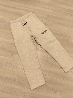 Grå mjukisbyxor från Essentials - Säljer ett par ljusgrå mjukisbyxor från Fear of God Essentials. Byxorna har resår i midjan med dragsko, sidofickor och svart logga tryckt på benet. Tillverkade i mjukt bomullsmaterial för maximal komfort.