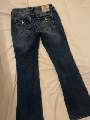 True religon mid rise  - Snygga true religon bootcut jeans mid rise i mörkblå denim med klassiska fickor och kontrastsömmar i gul. Jeansen har en lätt tvättad look framtill och bakfickor med lock och knapp. 
