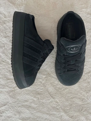 Adidas uggs/ sneakers med platåsula - Säljer ett par svarta Adidas sneakers/uggs med platåsula och klassiska tre ränder på sidan. Skorna har en låg silhuett, snörning och är tillverkade i mockaliknande material. Super populära, använda FÅTAL tillfällen vid torrt underlag 