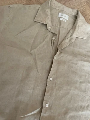Beige linneskjorta från Massimo Dutti  - Säljer en stilren beige skjorta från Massimo  i 100% linne. Skjortan har klassisk krage, knappar framtill och långa ärmar. Perfekt för en avslappnad men ändå snygg look. Passar till både jeans och shorts.