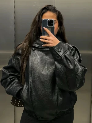 Zara Oversized svart skinnjacka - HELT NY MED PRISLAPP Säljer en oversized svart skinnjacka med breda axlar och coola detaljer som knappar vid kragen och axlarna. Jackan har en slät, glansig finish och en avslappnad passform som ger en edgy look. Perfekt för dig som vill sticka ut med en trendig streetstyle.