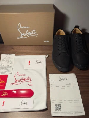 Svarta sneakers från Christian Louboutin - Snygga svarta sneakers från Christian Louboutin med klassisk låg profil och svarta skosnören. Skorna har en stilren design i läder med beige innerfoder och kommer med originalkartong, dustbag och tillbehör. Perfekta för dig som gillar exklusiva detaljer.