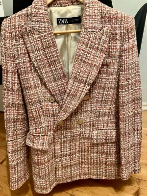 Tweedkavaj i rosa och beige från Zara - Snygg dubbelknäppt kavaj från Zara i tweedmaterial med rosa, beige och vita toner. Klassisk modell med breda slag, två framfickor med lock och guldfärgade knappar. Perfekt för dig som vill ha en trendig och stilren look.