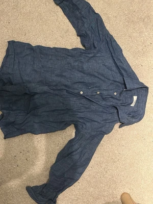 Blå linneskjorta från Uniqlo - Snygg blå skjorta från Uniqlo i luftigt linne. Klassisk krage, knäppning framtill och långa ärmar. Perfekt för dig som gillar en avslappnad men stilren look. Passar till både jeans och chinos.