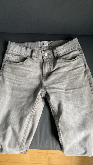 Grå jeans från 157 med rak passform - Säljer ett par grå jeans från 157 med klassisk femficksmodell och rak passform. Jeansen har bälteshällor, knappgylf och är tillverkade i ett mjukt denimtyg. Perfekta för en avslappnad och stilren look.