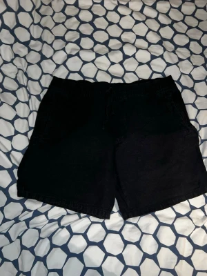 Svarta denimshorts med dragsko - Säljer ett par svarta shorts i denim med elastisk midja och dragsko. Shortsen har två fickor fram och en bakficka. Perfekta för en avslappnad och stilren look. Passar till det mesta och är riktigt bekväma.