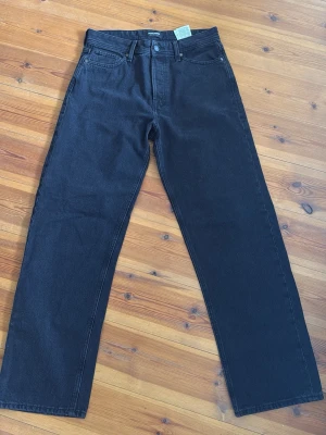 Svarta jeans från Jack and Jones - Säljer ett par svarta jeans från Jack and Jones med loose passform och klassisk femficksdesign. Jeansen har hög midja och är tillverkade i kraftig denim. Perfekta för dig som gillar en clean och stilren look.