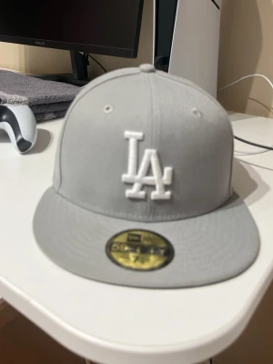 Grå LA New Era 59Fifty keps - Snygg grå fitted keps från New Era med LA Dodgers-logga broderad i vitt framtill. Klassisk 59Fifty-modell med platt skärm och MLB-logga baktill. Tillverkad i bomullsmix för skön passform och stilren look.