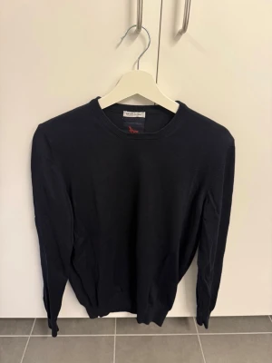 Svart stickad tröja från Gran Sasso, stl S/50 - Klassisk svart stickad tröja från Gran Sasso med rund halsringning och långa ärmar. Tröjan har ribbade muddar vid ärmslut och nederkant. Perfekt att bära över en skjorta för en stilren look.