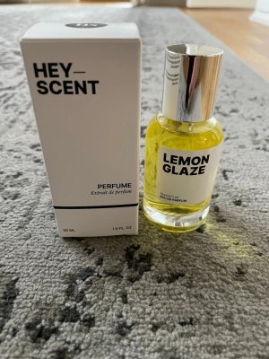 HEY SCENT Lemon Glaze parfym 30 ml - Fräsch parfym från HEY SCENT med doften Lemon Glaze. Flaskan är rund i genomskinligt glas med silverfärgat lock och gul vätska. Medföljande vit kartong med svart text. Perfekt för dig som gillar citrusdofter. Inspirerad av Casamorati Lira